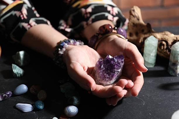 Hands holding vibrant deep purple amethyst crystals, surrounded by other healing stones and bracelets.