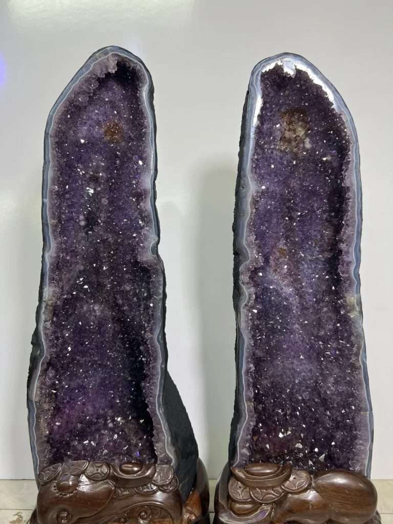 Museum-quality 121 lb matching Uruguayan amethyst twin towers known as the Twin Guardian Towers, featuring deep velvet purple crystals on custom carved wood stands
