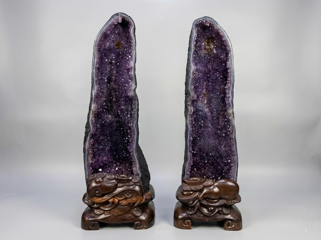 A pair of authentic large amethyst cathedral geodes on carved wooden stands